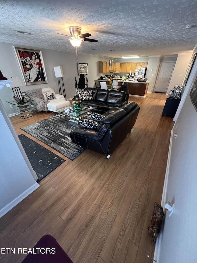 living room with visible vents, baseboards, a ceiling fan, wood finished floors, and a textured ceiling