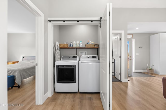 laundry area featuring laundry area, a barn door, baseboards, independent washer and dryer, and light wood-style floors