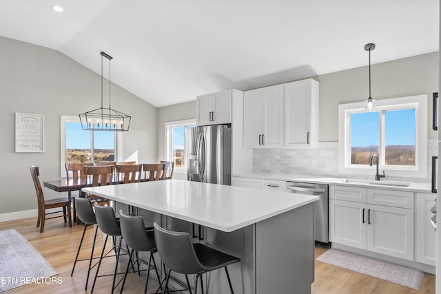 kitchen featuring light wood finished floors, lofted ceiling, a kitchen island, stainless steel appliances, and light countertops