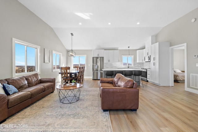 living room featuring high vaulted ceiling, recessed lighting, visible vents, and light wood finished floors