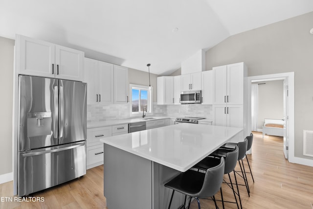 kitchen with backsplash, appliances with stainless steel finishes, white cabinets, vaulted ceiling, and a kitchen island