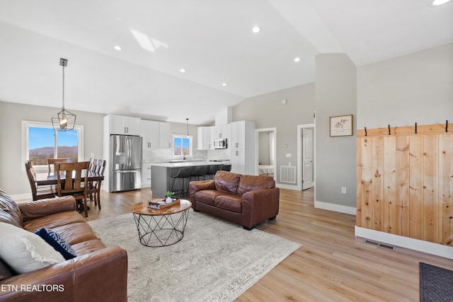 living room featuring lofted ceiling, light wood-style floors, baseboards, and visible vents