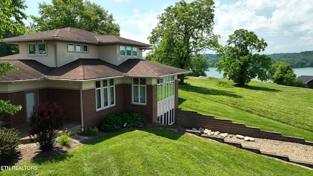 view of side of property featuring a yard, brick siding, roof with shingles, and a water view