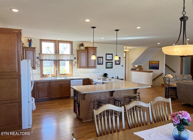 kitchen with a sink, white appliances, wood finished floors, and a kitchen bar