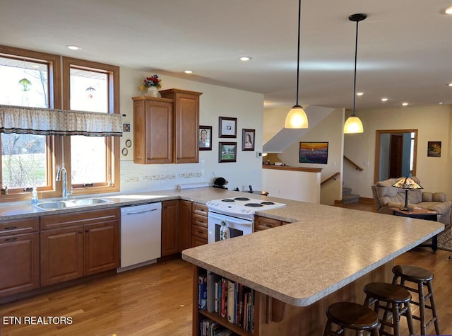 kitchen with white dishwasher, light wood-style flooring, a peninsula, a sink, and a kitchen breakfast bar