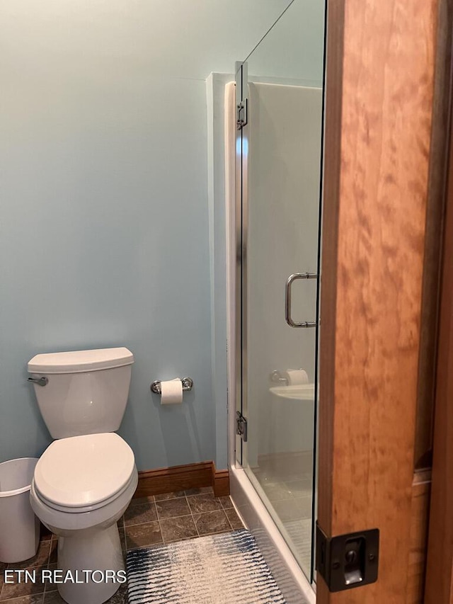 full bathroom with a stall shower, baseboards, and toilet