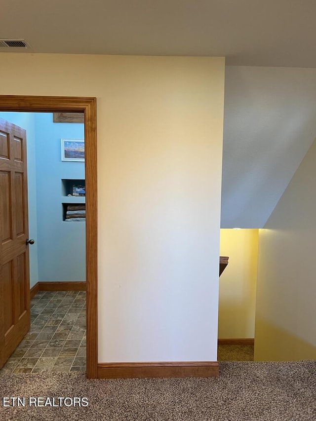 corridor with baseboards, visible vents, and dark colored carpet