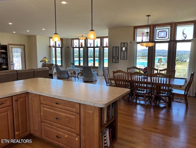 kitchen with dark wood-style floors, pendant lighting, light countertops, brown cabinetry, and open floor plan