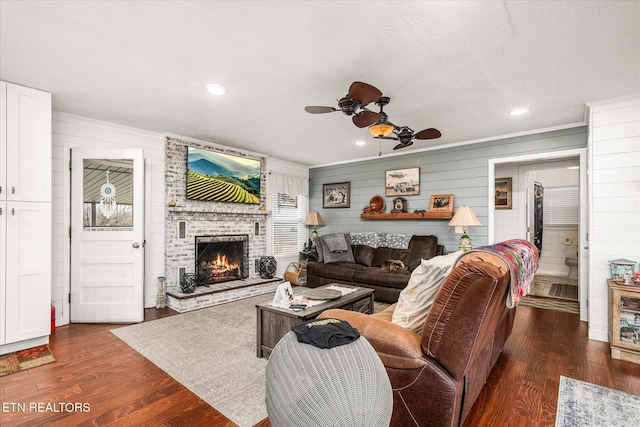 living room featuring a ceiling fan, dark wood-style floors, ornamental molding, a fireplace, and recessed lighting