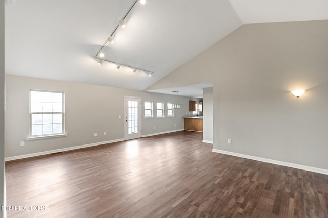 unfurnished living room with high vaulted ceiling, rail lighting, dark wood finished floors, and baseboards