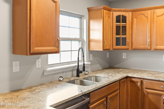 kitchen featuring glass insert cabinets, a sink, light stone counters, and stainless steel dishwasher