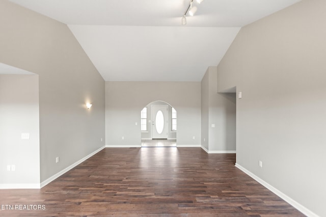 unfurnished living room featuring arched walkways, dark wood-type flooring, track lighting, high vaulted ceiling, and baseboards