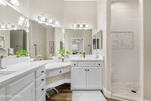 bathroom with two vanities, ceiling fan, a sink, wood finished floors, and a walk in shower