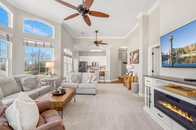 living area with crown molding, a glass covered fireplace, a towering ceiling, and light colored carpet