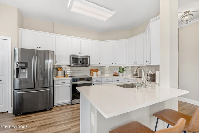 kitchen featuring a breakfast bar area, a peninsula, a sink, appliances with stainless steel finishes, and tasteful backsplash