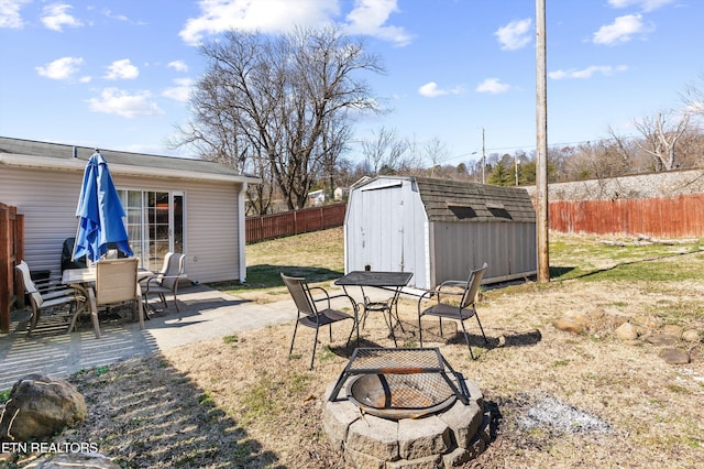 view of yard featuring outdoor dining space, fence, a fire pit, and a shed