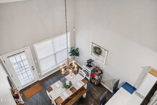 living area featuring an inviting chandelier, a high ceiling, baseboards, and wood finished floors