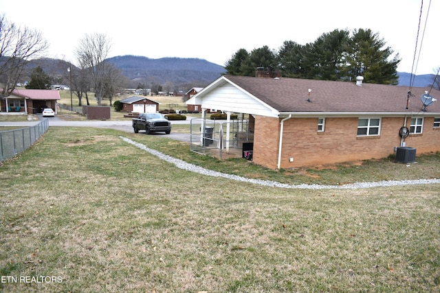 exterior space featuring a mountain view, brick siding, a shingled roof, fence, and a yard