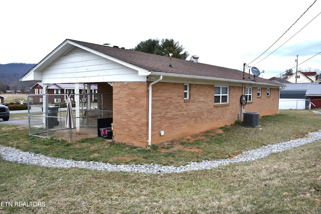 view of side of home with a shingled roof, central AC unit, a lawn, fence, and brick siding