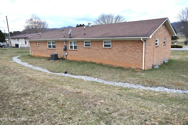 back of house with a yard, roof with shingles, cooling unit, and brick siding