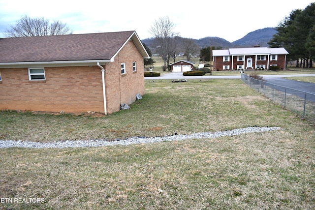 view of home's exterior featuring brick siding, a shingled roof, a lawn, a mountain view, and fence