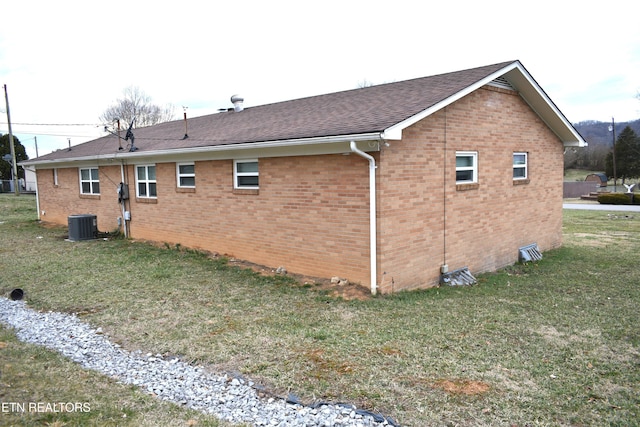 view of side of home with roof with shingles, brick siding, a lawn, and central air condition unit