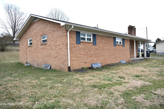 view of side of property featuring brick siding, a yard, and a chimney