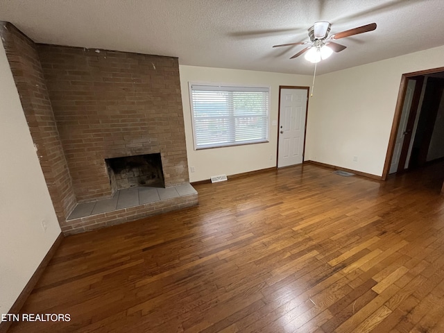 unfurnished living room with baseboards, visible vents, wood-type flooring, a textured ceiling, and a fireplace