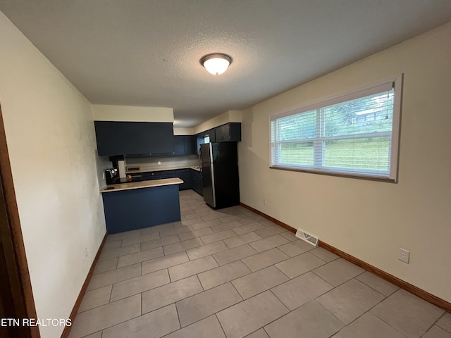 kitchen with visible vents, freestanding refrigerator, a peninsula, light countertops, and dark cabinetry