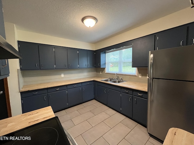 kitchen with light tile patterned floors, freestanding refrigerator, a sink, a textured ceiling, and extractor fan