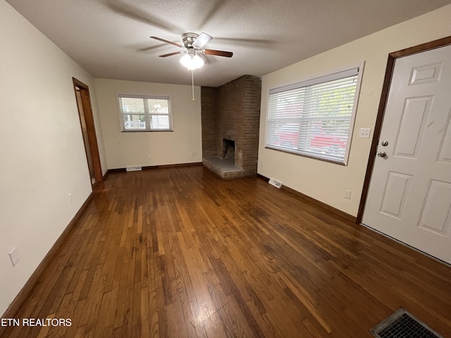 unfurnished living room featuring a fireplace, visible vents, dark wood finished floors, and a textured ceiling