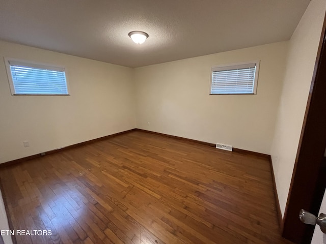 unfurnished room with baseboards, a textured ceiling, visible vents, and hardwood / wood-style floors