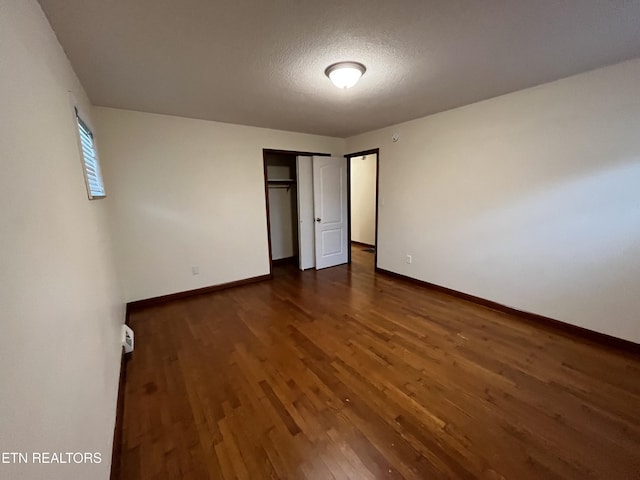 unfurnished bedroom with a closet, dark wood-style flooring, a textured ceiling, and baseboards