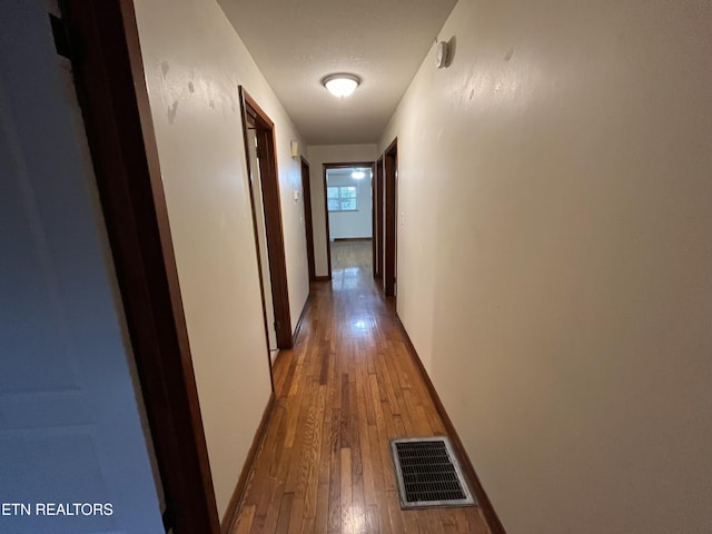 corridor with light wood-style flooring, visible vents, and baseboards