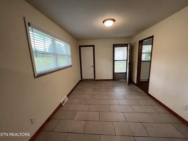 empty room featuring tile patterned flooring, a textured ceiling, and baseboards