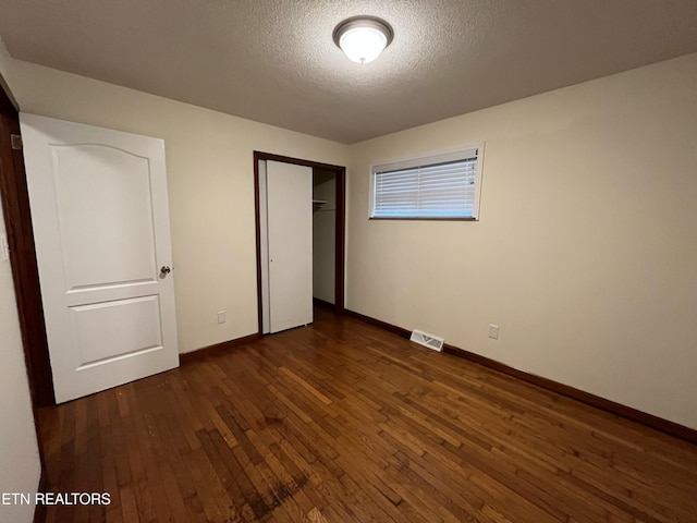 unfurnished bedroom with baseboards, visible vents, dark wood-type flooring, a textured ceiling, and a closet