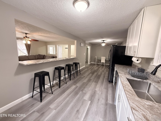 kitchen with a ceiling fan, a sink, light wood-style floors, white cabinetry, and a kitchen breakfast bar