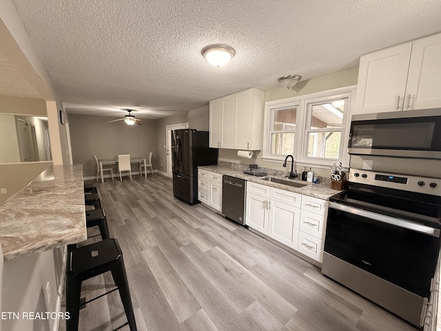 kitchen featuring light stone counters, light wood-style flooring, a sink, stainless steel appliances, and white cabinets