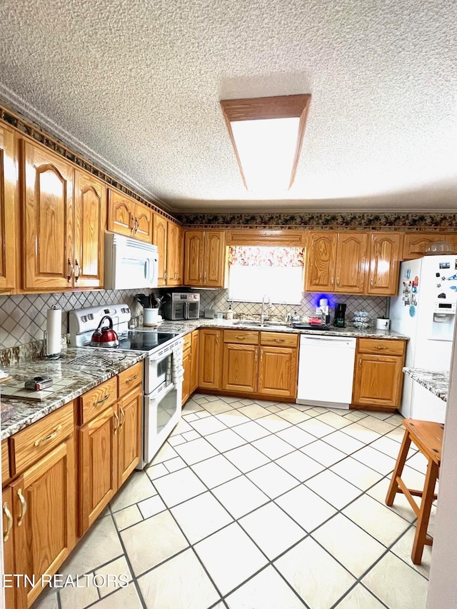 kitchen featuring white appliances, light stone countertops, a sink, decorative backsplash, and brown cabinets