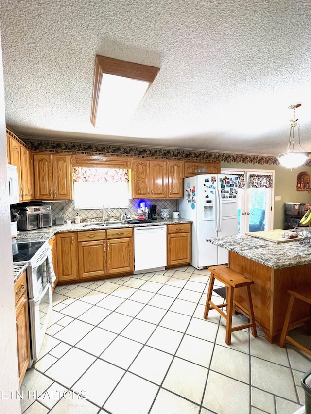 kitchen featuring tasteful backsplash, white appliances, brown cabinetry, and a sink