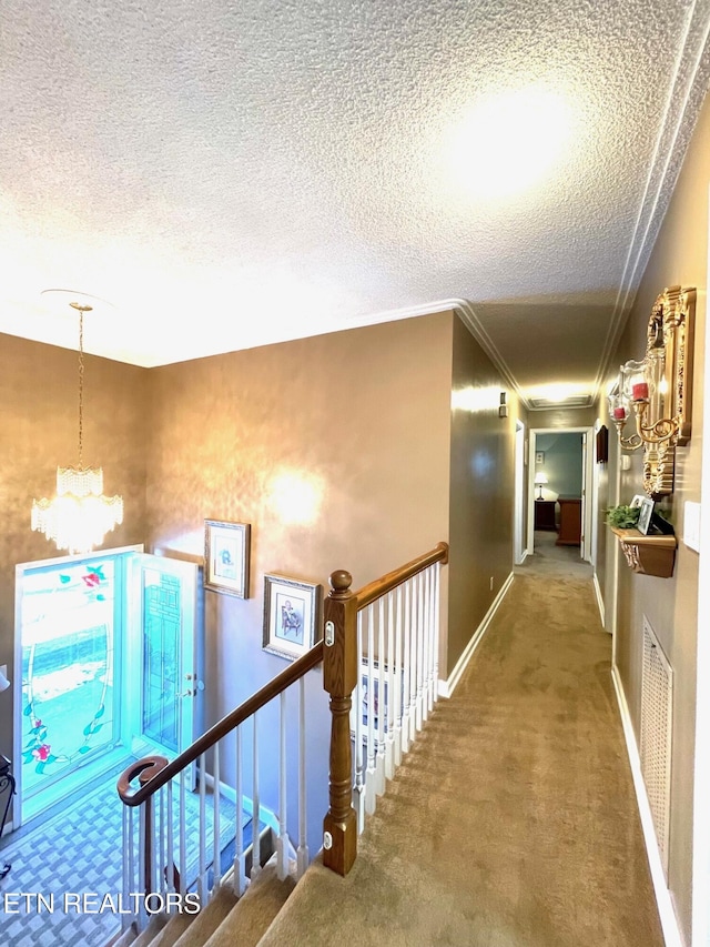 hall featuring visible vents, an upstairs landing, a textured ceiling, an inviting chandelier, and carpet flooring