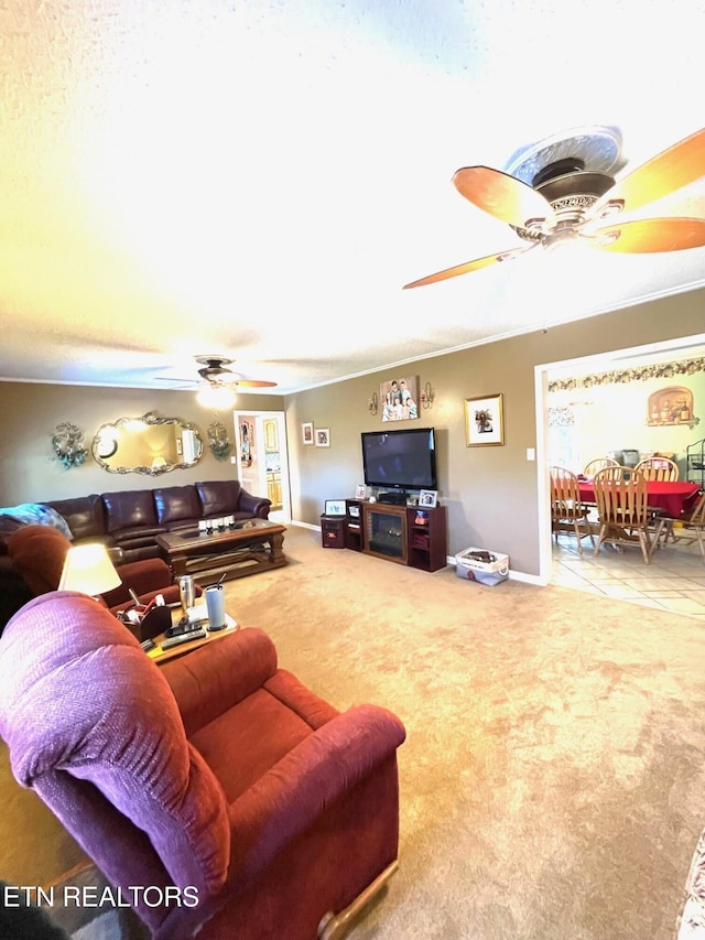 carpeted living area featuring baseboards, ornamental molding, and a ceiling fan