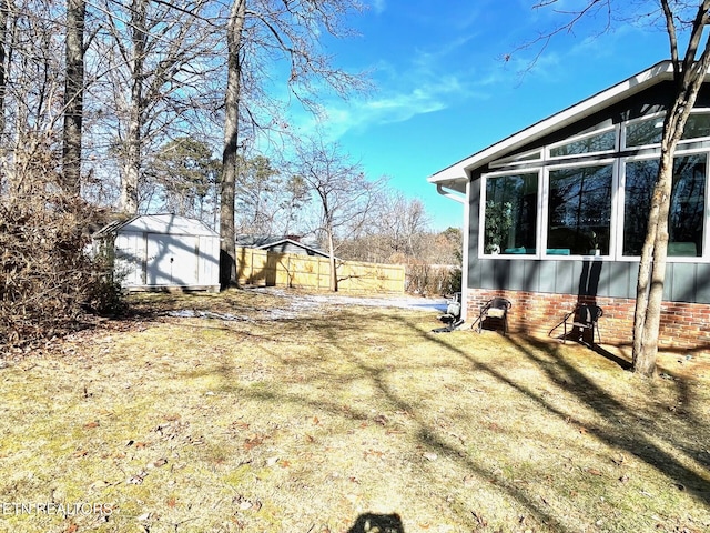 view of yard featuring a storage shed, an outdoor structure, fence, and a sunroom