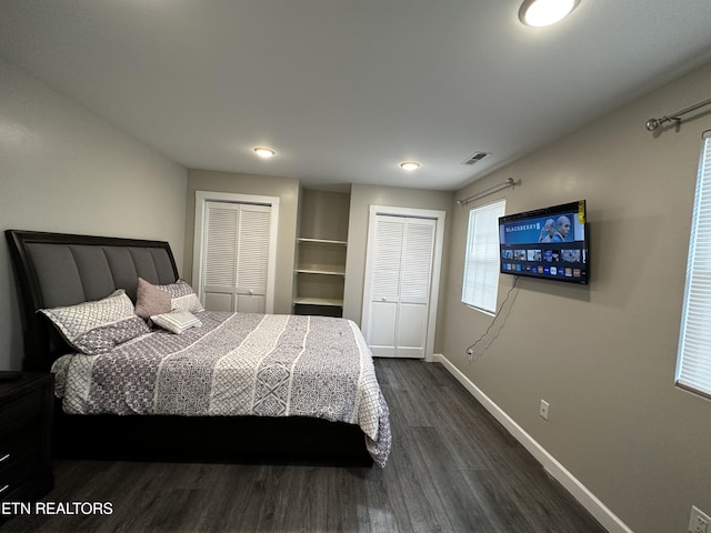 bedroom with multiple closets, visible vents, dark wood finished floors, and baseboards