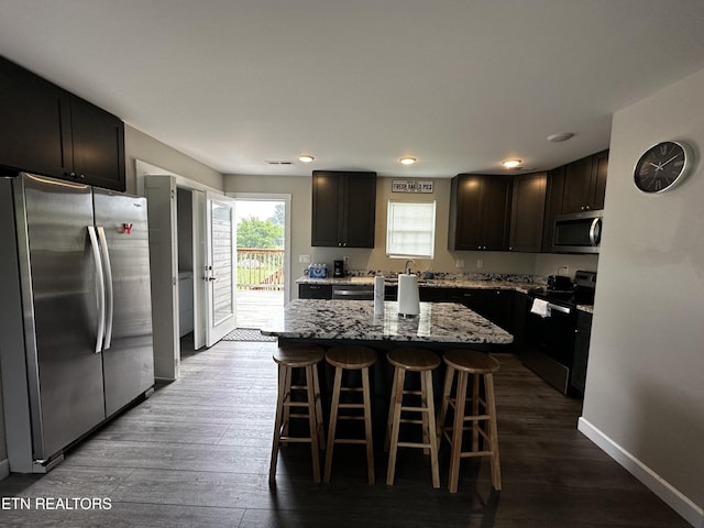 kitchen featuring baseboards, dark wood-style floors, a breakfast bar, light stone countertops, and stainless steel appliances