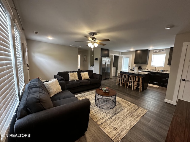 living room featuring dark wood-style flooring, visible vents, and a ceiling fan