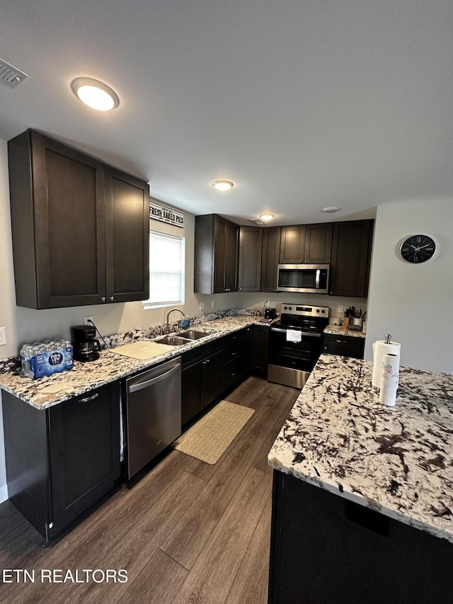 kitchen with visible vents, light stone counters, dark wood-style flooring, stainless steel appliances, and a sink