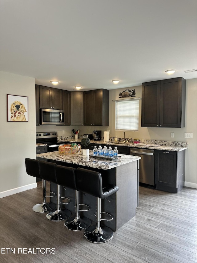 kitchen with light stone countertops, a kitchen bar, appliances with stainless steel finishes, and a center island