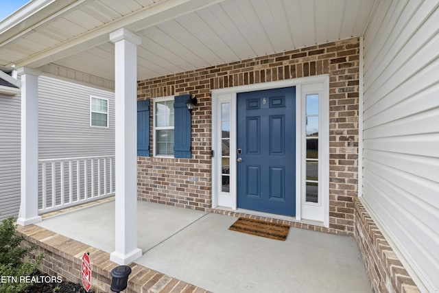 doorway to property featuring a porch and brick siding