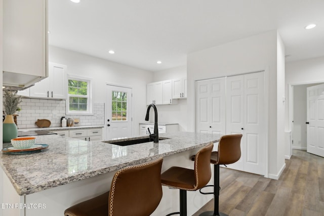 kitchen with a kitchen breakfast bar, tasteful backsplash, white cabinets, wood finished floors, and light stone counters